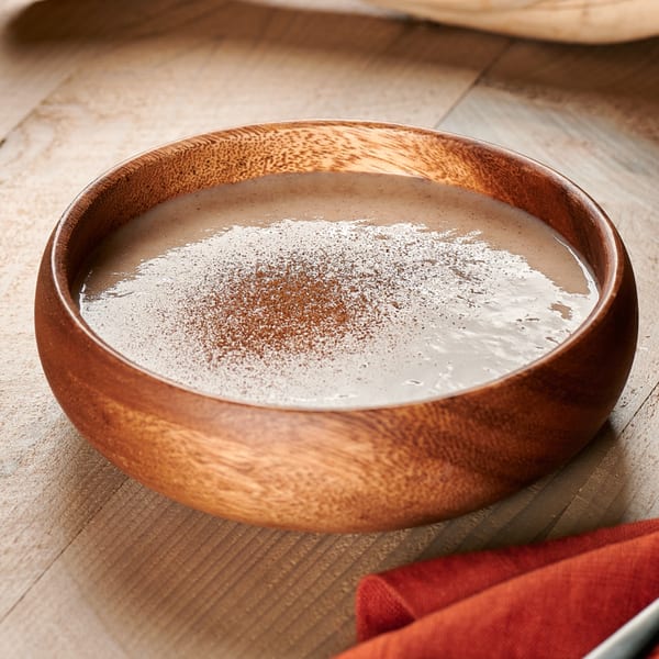 Creamy Jamaican porridge with a sprinkle of cinnamon in a wooden bowl on a wooden table.