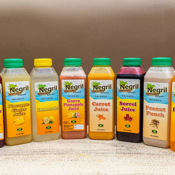 A row of Negril Jamaican Restaurant bottled juices, including pineapple ginger, lemonade, guava pineapple, carrot, sorrel, and peanut punch.