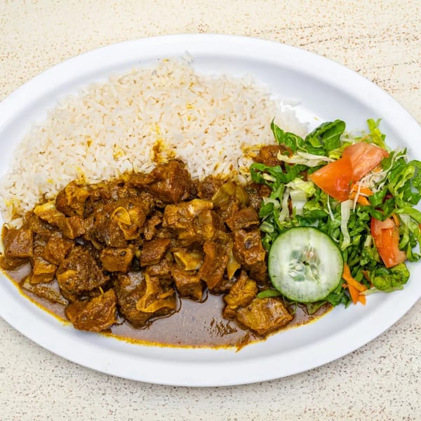A plate of Negril Jamaican curry goat with white rice and a side salad.