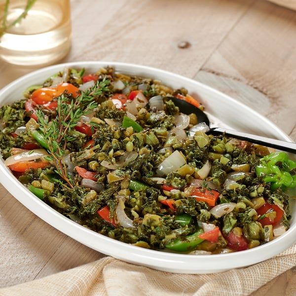 A white oval dish filled with callaloo, bell peppers, onions, and tomatoes, garnished with thyme.