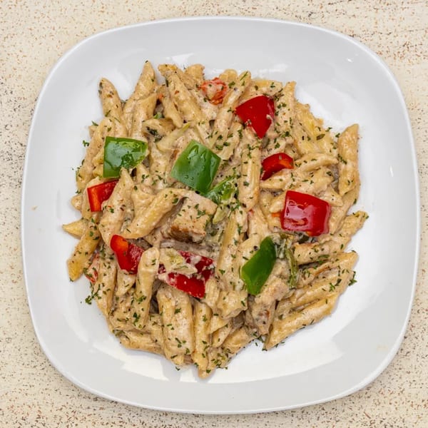 Creamy penne pasta with chicken, red and green bell peppers, and parsley on a white plate.